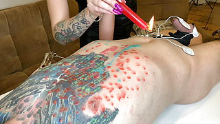 Hot wax for the body of a slave. Dominatrix Nika pours hot wax from a candle on the slave's chest.